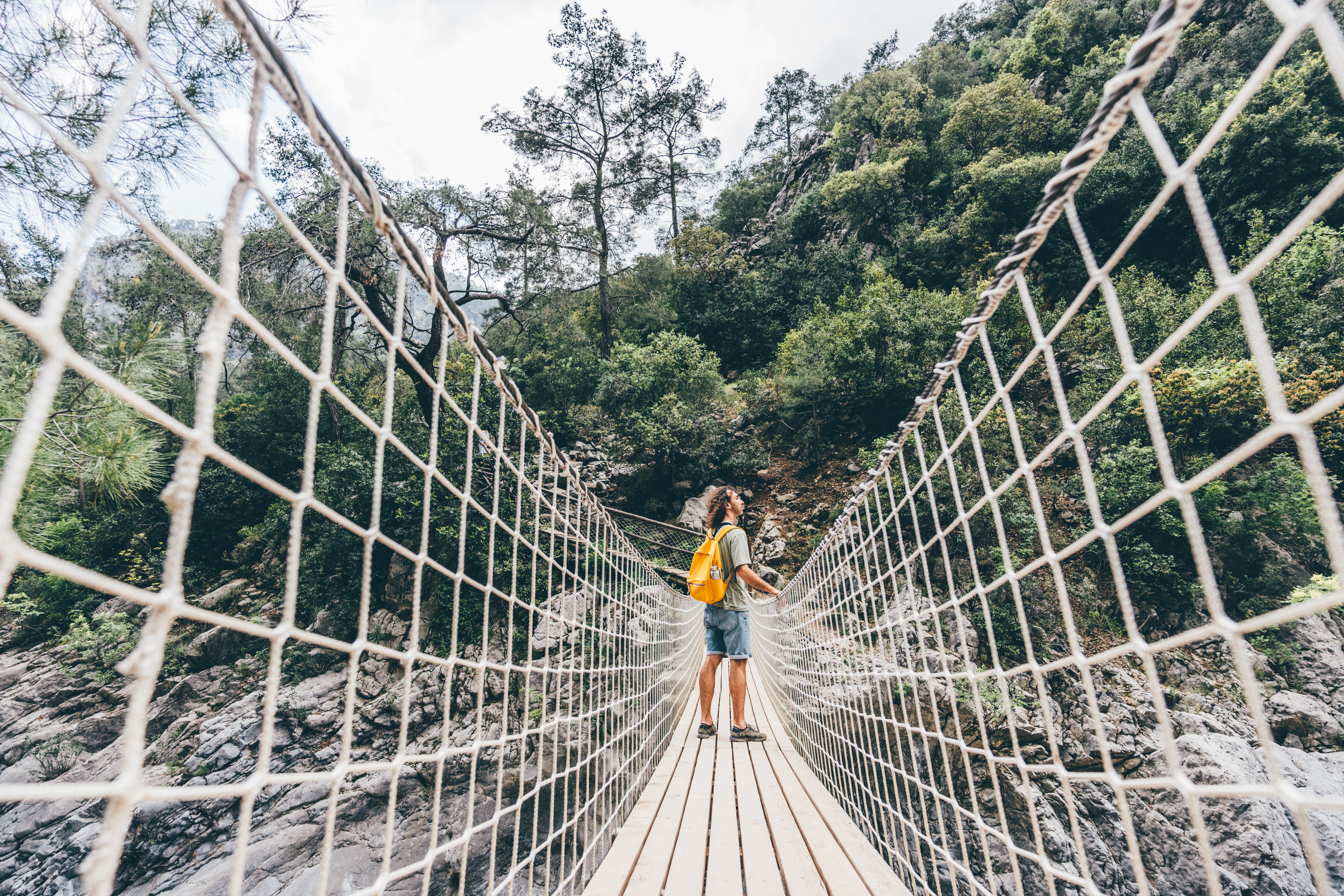 Young woman crossing a suspension bridge over mountain stream.